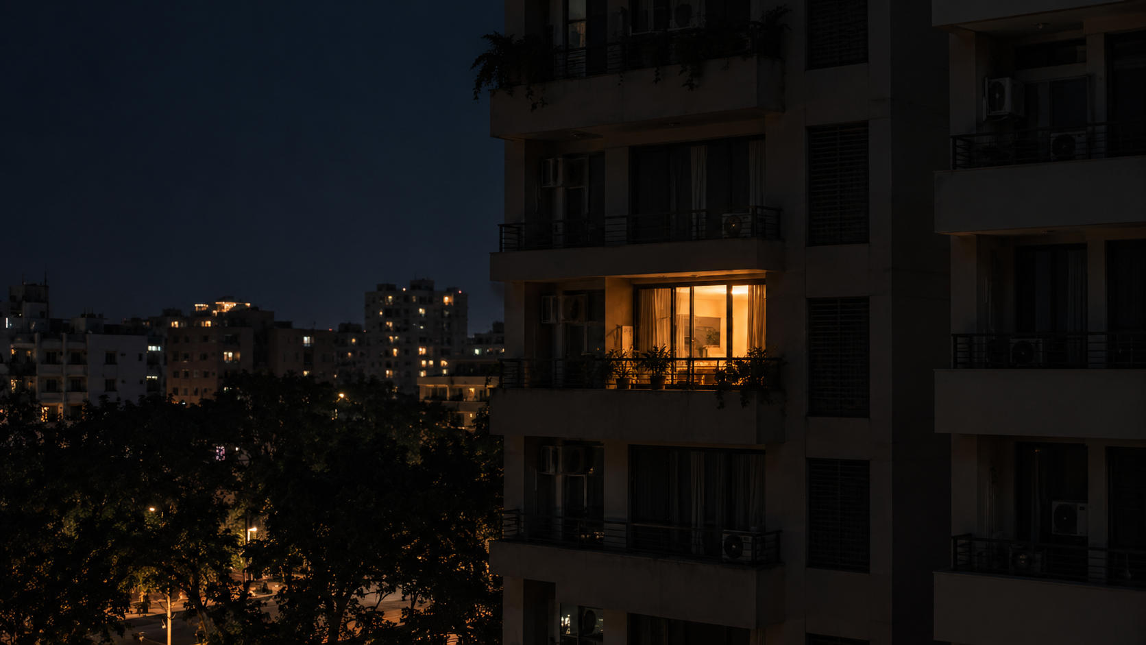 An apartment building at night with almost every window dark and one glowing warm